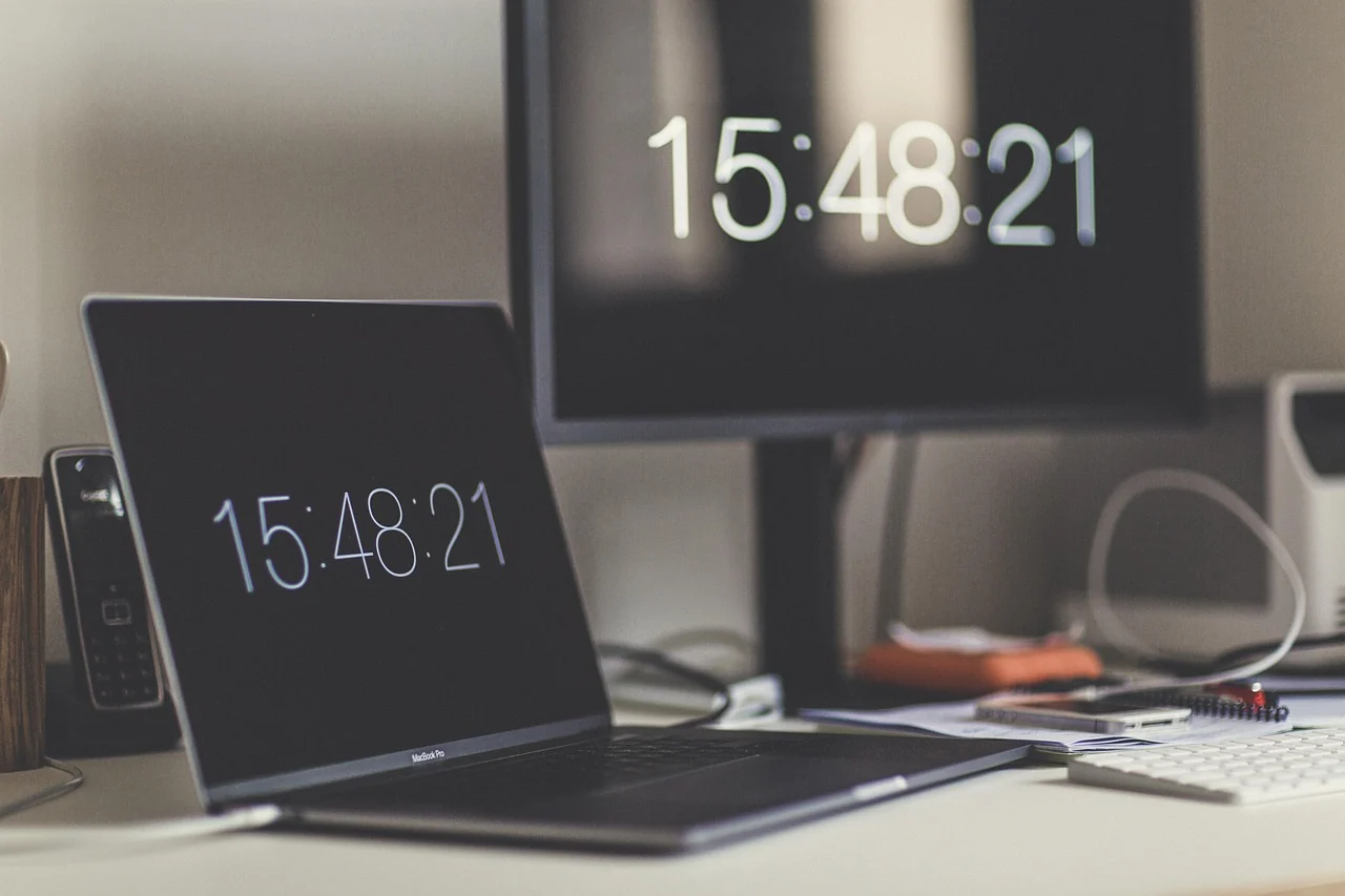 A laptop and desktop display showing clock screensavers on a desk
