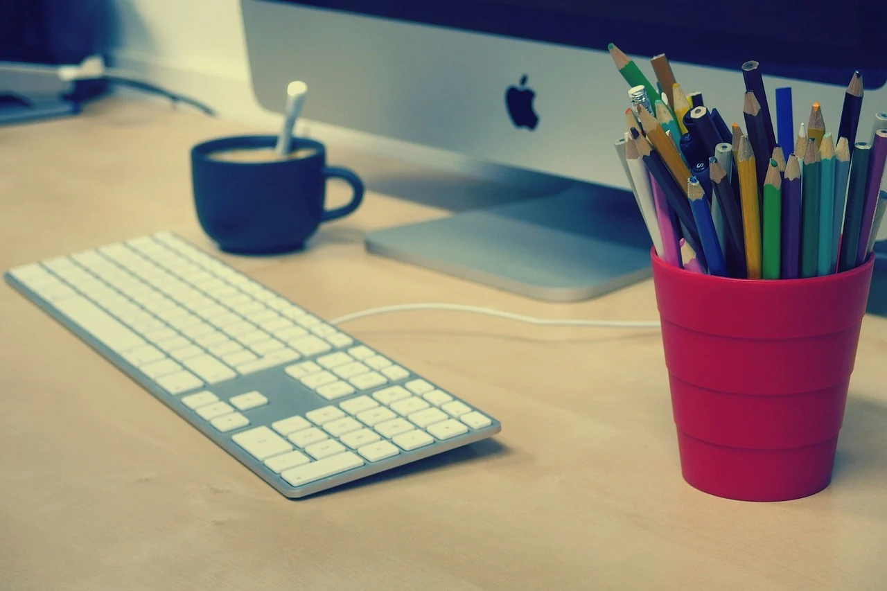 Keyboard, cup and pencil pot beside a desktop computer