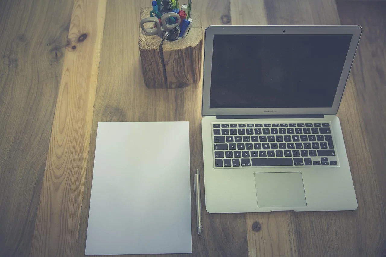 Laptop, blank paper and stationery arranged on a wooden desk